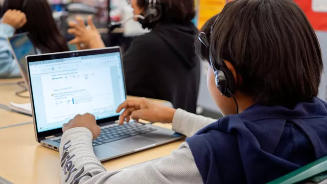 Young male student wearing headphones and doing school work on a laptop.