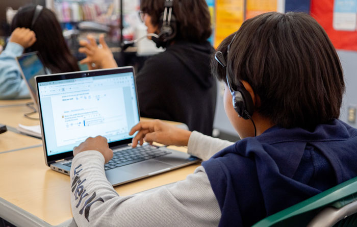 Young male student wearing headphones and doing school work on a laptop.